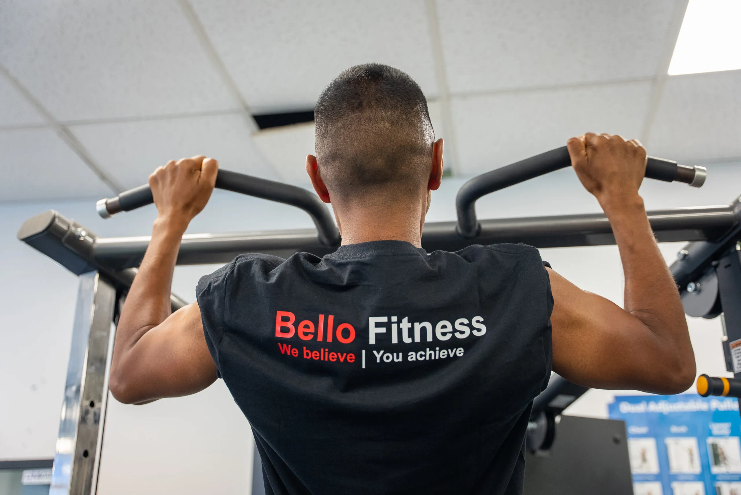A learner in a Bello Fitness shirt training at the pull-up bar